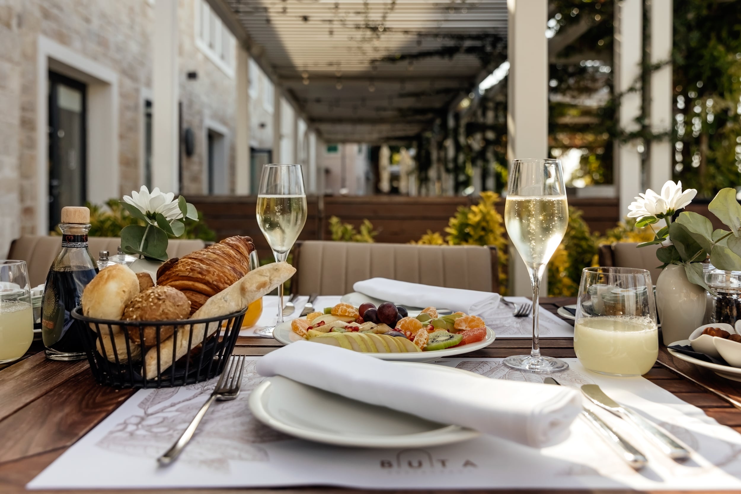 Breakfast table at Buta with dishes, bread, and glasses on the terrace.